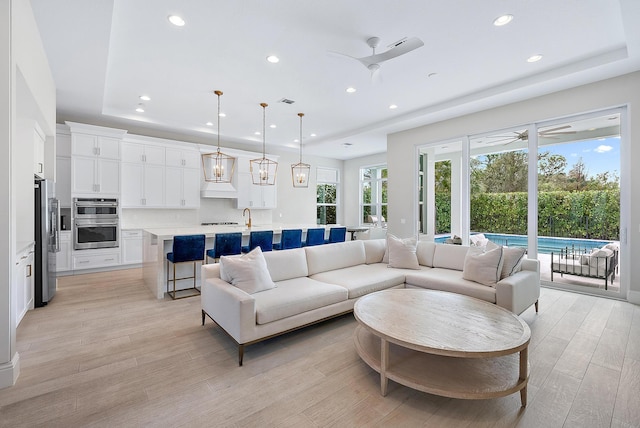 living room with sink, ceiling fan, a tray ceiling, and light hardwood / wood-style flooring