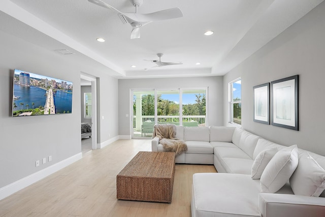 living room featuring ceiling fan, a raised ceiling, and light hardwood / wood-style flooring