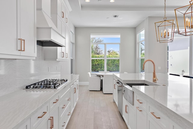 kitchen with hanging light fixtures, stainless steel appliances, custom exhaust hood, white cabinetry, and light stone counters