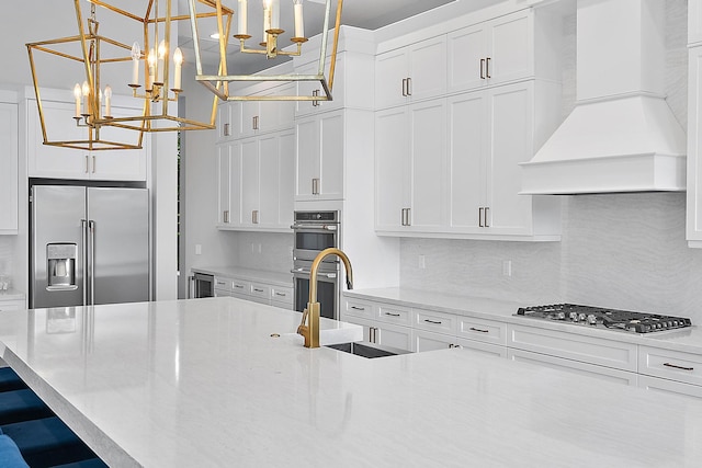 kitchen featuring premium range hood, appliances with stainless steel finishes, hanging light fixtures, and white cabinetry