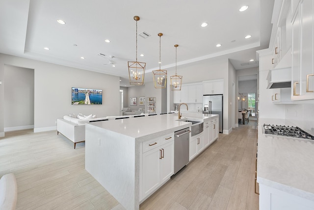 kitchen featuring a large island with sink, sink, white cabinets, and hanging light fixtures