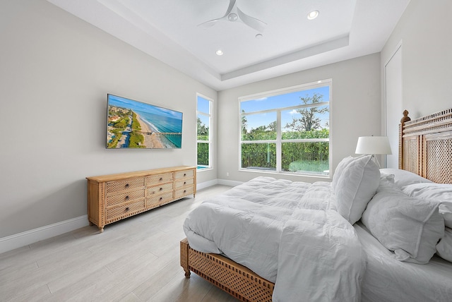 bedroom with light hardwood / wood-style floors, a tray ceiling, and ceiling fan