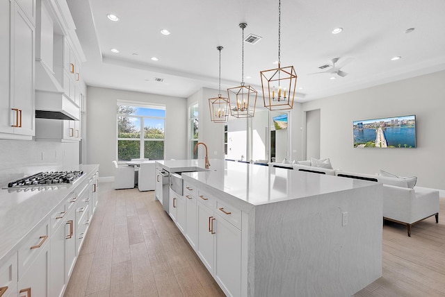 kitchen featuring sink, light wood-type flooring, a spacious island, hanging light fixtures, and white cabinets