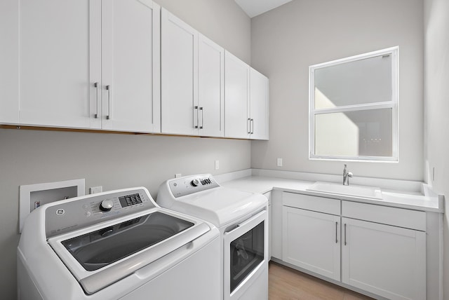 washroom with washing machine and dryer, sink, light wood-type flooring, and cabinets