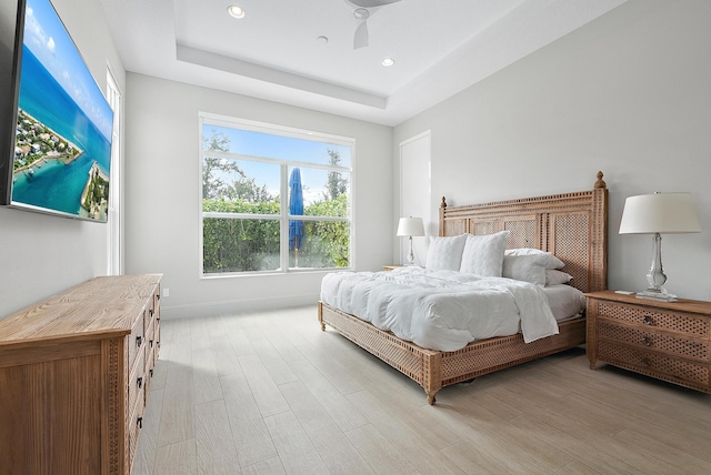 bedroom featuring light hardwood / wood-style flooring, a tray ceiling, and ceiling fan