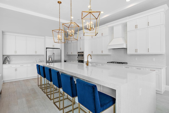 kitchen featuring a spacious island, premium range hood, stainless steel appliances, and hanging light fixtures