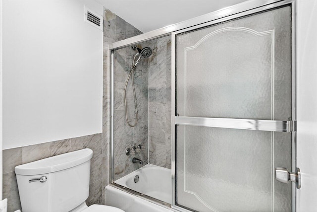 bathroom featuring tile walls, shower / bath combination with glass door, and toilet