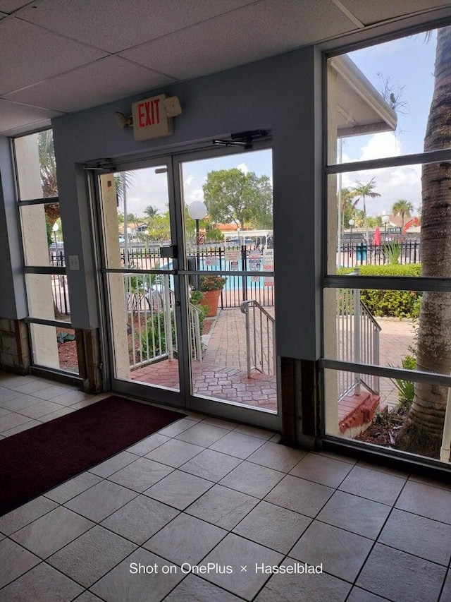 doorway to outside featuring a paneled ceiling, a water view, and light tile patterned floors