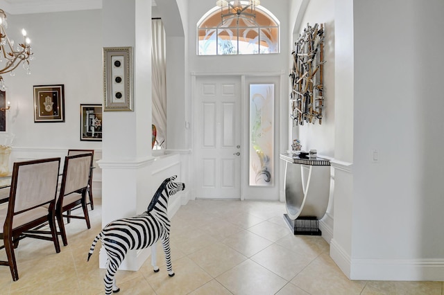 entryway with ornate columns, light tile patterned floors, a high ceiling, and a chandelier