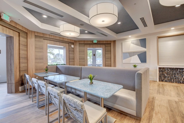 dining area with a tray ceiling, light hardwood / wood-style flooring, and wooden walls