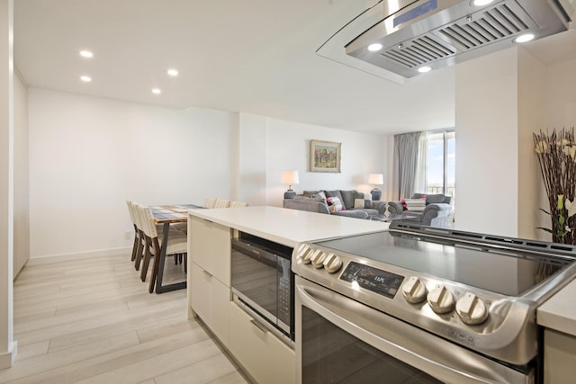 kitchen featuring light wood-style floors, wall chimney range hood, built in microwave, light countertops, and stainless steel range with electric stovetop