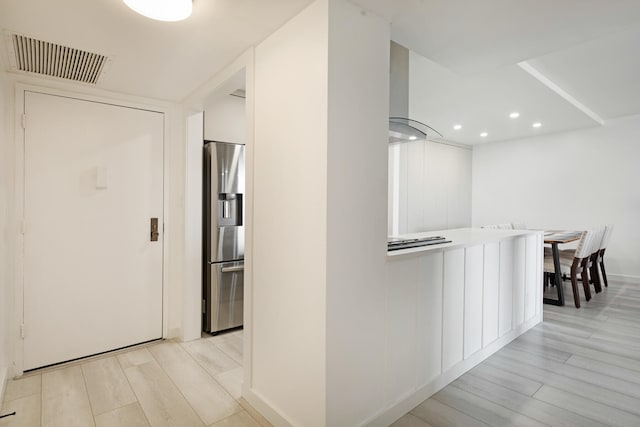 kitchen featuring white cabinets, wall chimney range hood, light hardwood / wood-style flooring, and stainless steel fridge