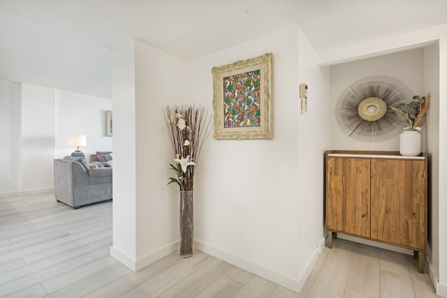 hall featuring light wood-style flooring and baseboards