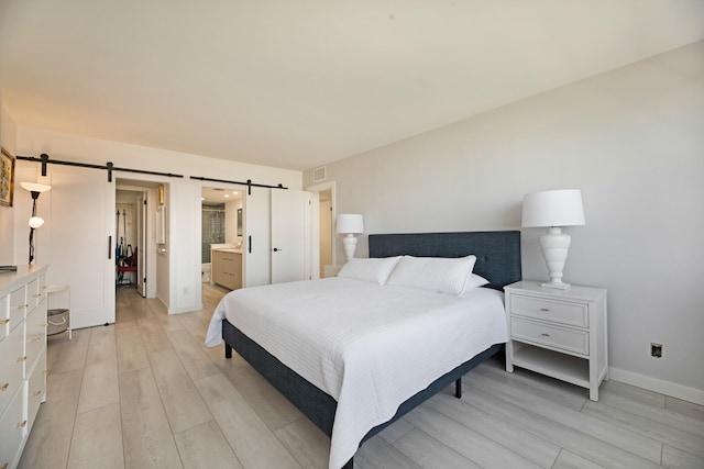 bedroom featuring light hardwood / wood-style floors, a barn door, and connected bathroom