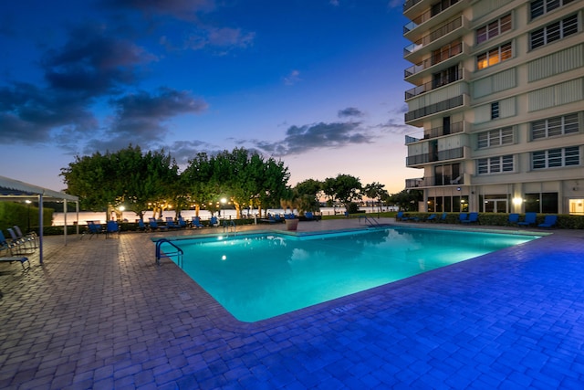 pool at dusk featuring a patio and a community pool