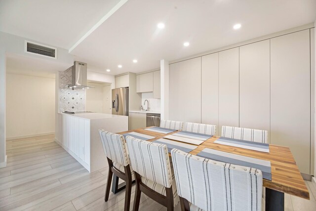 kitchen with light hardwood / wood-style floors, stainless steel appliances, and wall chimney range hood