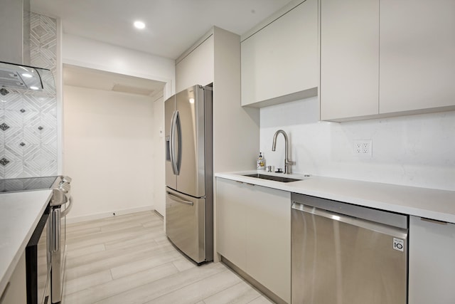 kitchen with wall chimney exhaust hood, stainless steel appliances, sink, white cabinets, and light hardwood / wood-style floors