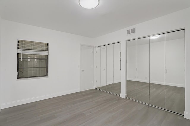 unfurnished bedroom with hardwood / wood-style floors and multiple closets