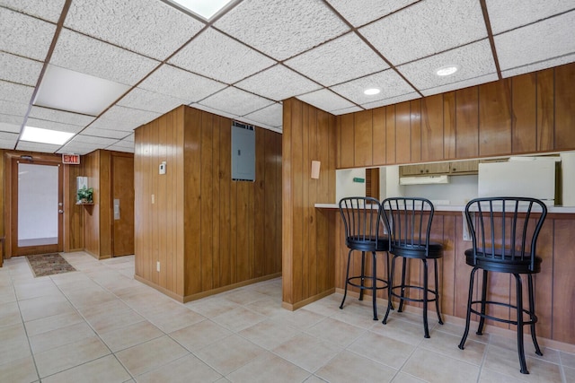 kitchen featuring a kitchen bar, fridge, wooden walls, kitchen peninsula, and a drop ceiling