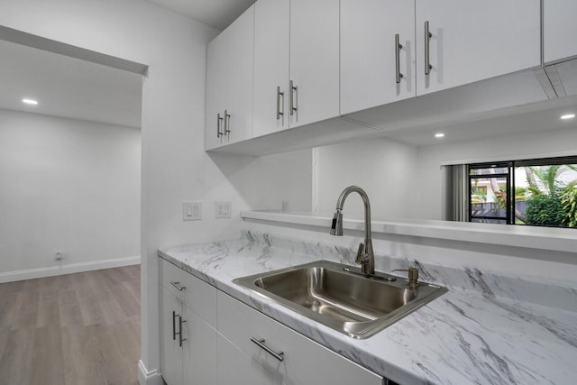 kitchen featuring light wood-type flooring, sink, light stone counters, and white cabinets