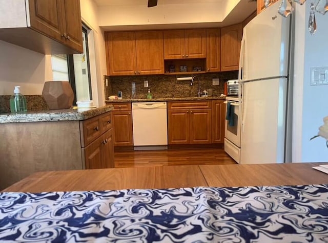 kitchen with sink, light wood-type flooring, white appliances, and dark stone countertops