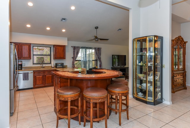 kitchen featuring sink, light tile patterned flooring, a kitchen bar, appliances with stainless steel finishes, and ceiling fan