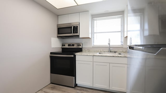 kitchen with tasteful backsplash, sink, light wood-type flooring, white cabinetry, and stainless steel appliances