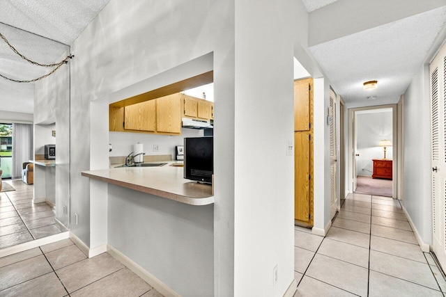 kitchen featuring sink, a textured ceiling, light tile patterned floors, and kitchen peninsula