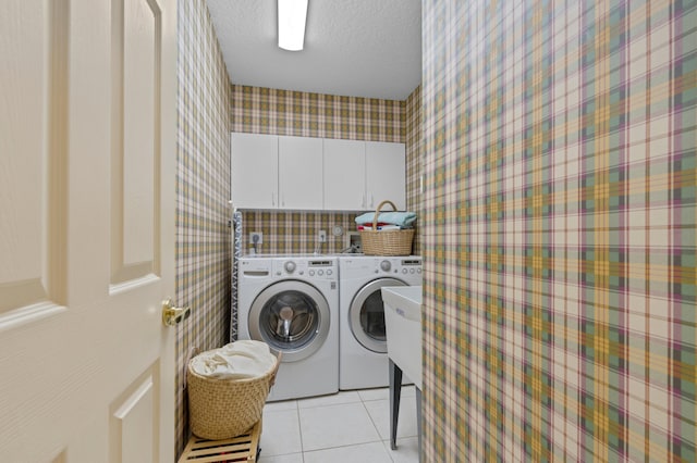 laundry room with a textured ceiling, washing machine and clothes dryer, cabinets, and light tile patterned floors