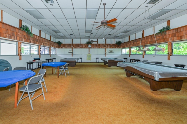 recreation room featuring ceiling fan, a healthy amount of sunlight, light carpet, and a drop ceiling