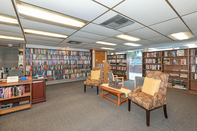 living area featuring a drop ceiling and dark carpet