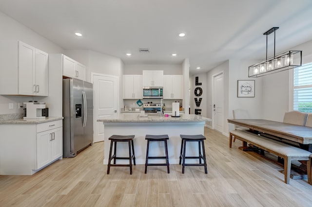 kitchen with a center island with sink, white cabinets, hanging light fixtures, light wood-type flooring, and appliances with stainless steel finishes