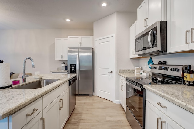 kitchen with light hardwood / wood-style floors, light stone counters, sink, white cabinetry, and appliances with stainless steel finishes