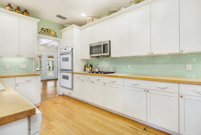 5400 Essex Ct, West Palm Beach, FL 33405 - kitchen with backsplash, white cabinetry, light wood-type flooring, and appliances with stainless steel finishes