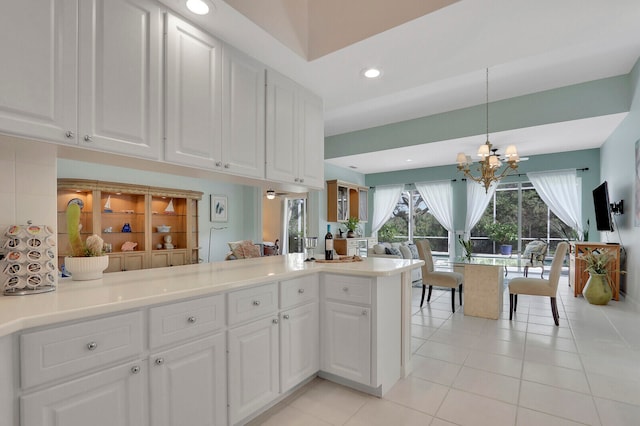 kitchen featuring kitchen peninsula, white cabinets, hanging light fixtures, light tile patterned floors, and a notable chandelier