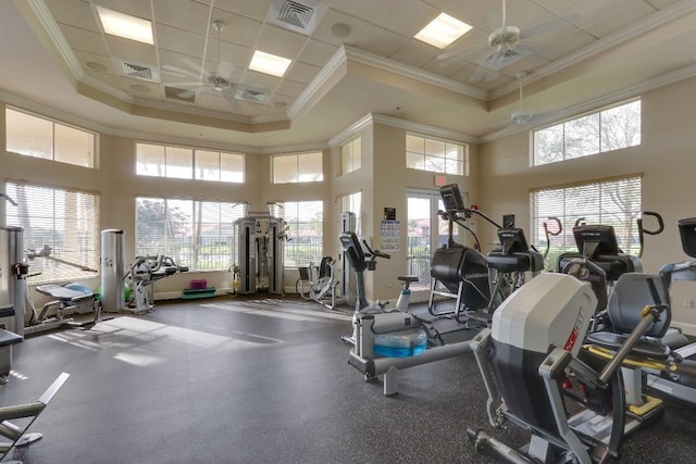 exercise room with a tray ceiling, ceiling fan, a healthy amount of sunlight, and ornamental molding