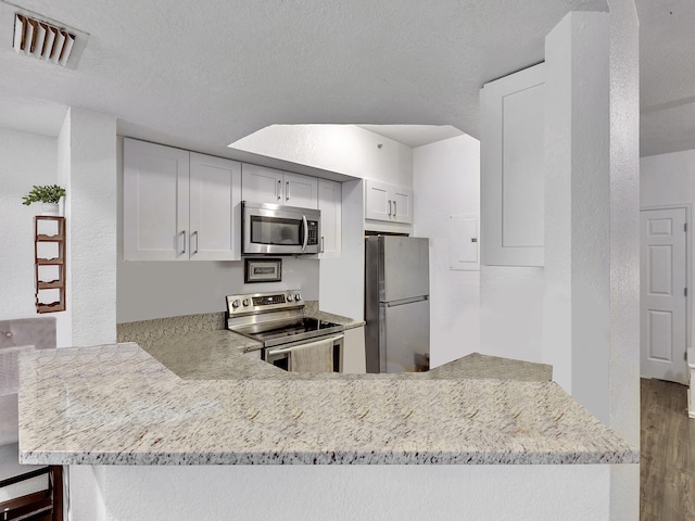 kitchen with hardwood / wood-style flooring, appliances with stainless steel finishes, kitchen peninsula, and white cabinets