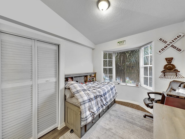 bedroom featuring lofted ceiling, hardwood / wood-style floors, a textured ceiling, and a closet