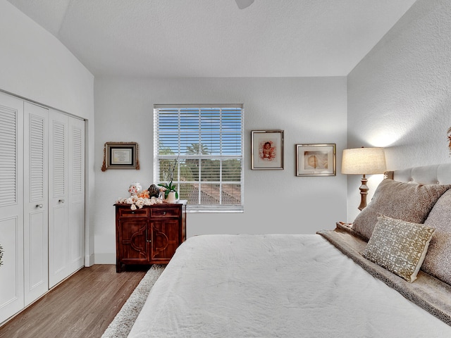 bedroom featuring a closet, light hardwood / wood-style floors, a textured ceiling, and lofted ceiling