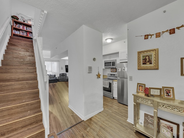 kitchen featuring light hardwood / wood-style flooring, white cabinetry, stainless steel appliances, and a textured ceiling