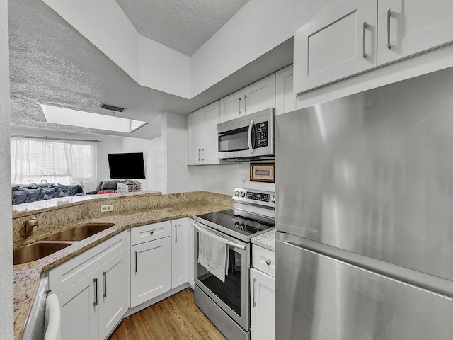 kitchen with appliances with stainless steel finishes, white cabinets, sink, and light hardwood / wood-style floors