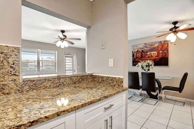 kitchen with ceiling fan, light stone counters, light tile patterned floors, and white cabinets