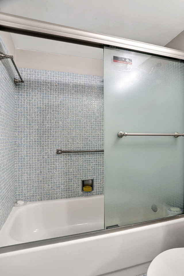 bathroom featuring toilet and shower / bath combination with glass door