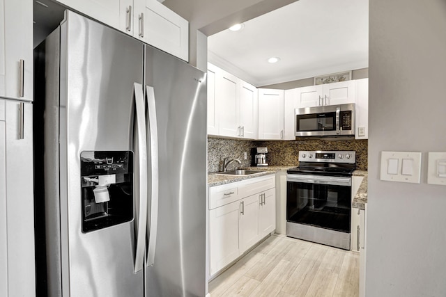 kitchen with appliances with stainless steel finishes, white cabinetry, light stone countertops, light hardwood / wood-style floors, and sink