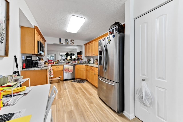 kitchen with kitchen peninsula, a textured ceiling, sink, light hardwood / wood-style floors, and stainless steel appliances