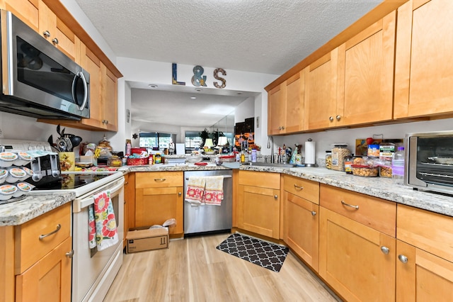 kitchen with sink, appliances with stainless steel finishes, a textured ceiling, and light hardwood / wood-style floors