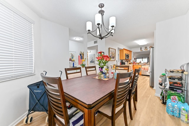 dining area featuring light hardwood / wood-style floors, a notable chandelier, and a textured ceiling