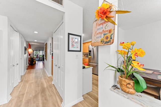 corridor featuring a textured ceiling and light hardwood / wood-style flooring