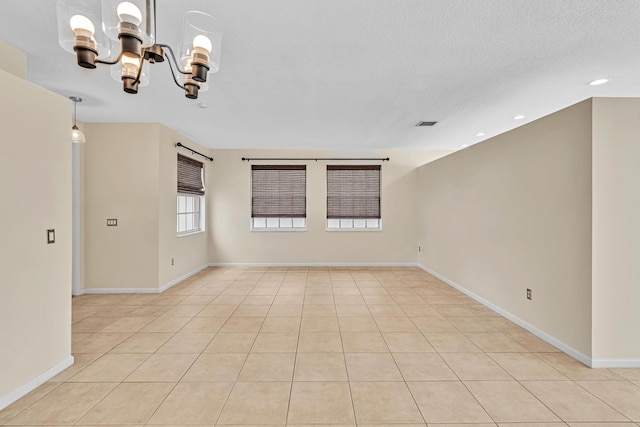 tiled spare room with a textured ceiling and an inviting chandelier