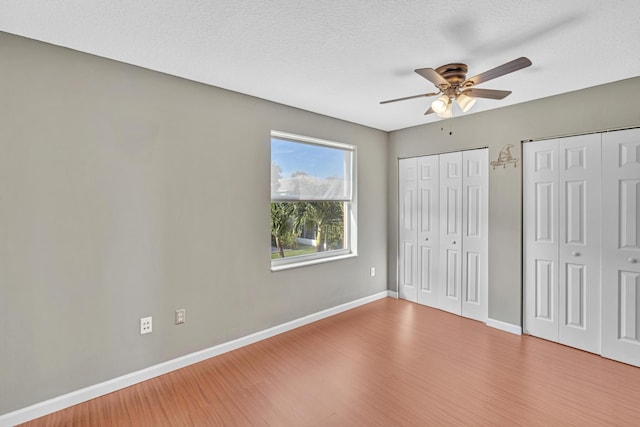 unfurnished bedroom featuring ceiling fan, multiple closets, a textured ceiling, and hardwood / wood-style floors